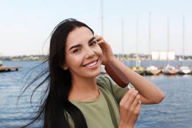 Photo of Beautiful young woman holding ice cream glazed in chocolate near river