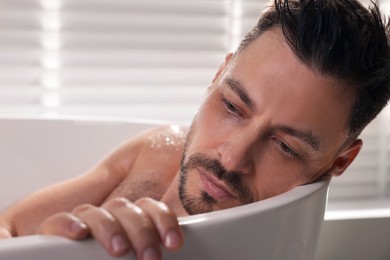 Upset man thinking about something in bathtub at home, closeup. Loneliness concept