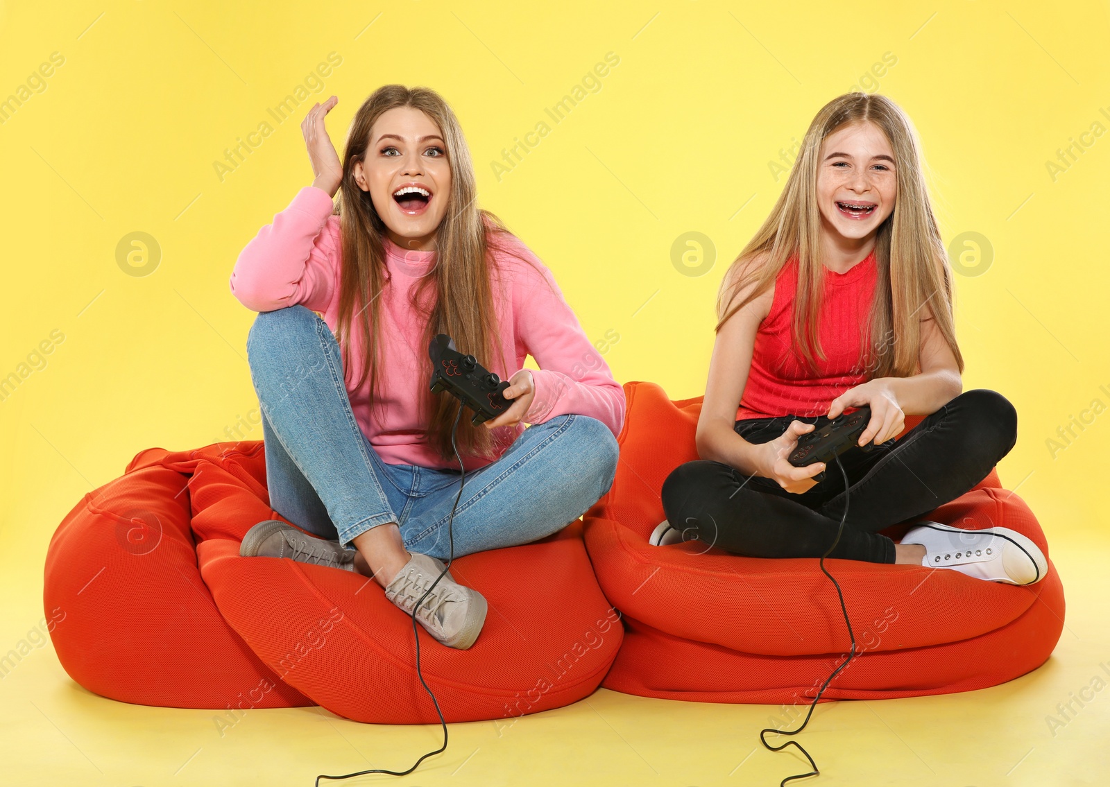 Photo of Young woman and teenage girl playing video games with controllers on color background