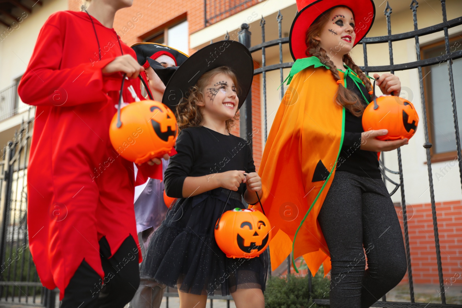 Photo of Cute little kids wearing Halloween costumes going trick-or-treating outdoors