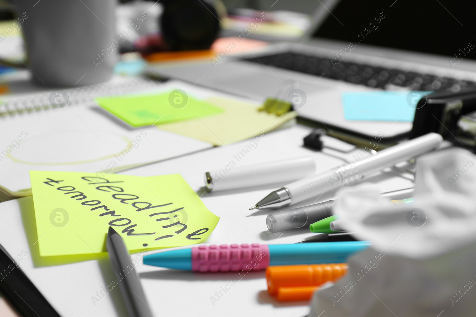 Photo of Messy table with laptop and stationery, closeup. Concept of being overwhelmed by work