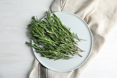 Photo of Plate with fresh rosemary twigs on wooden table, top view