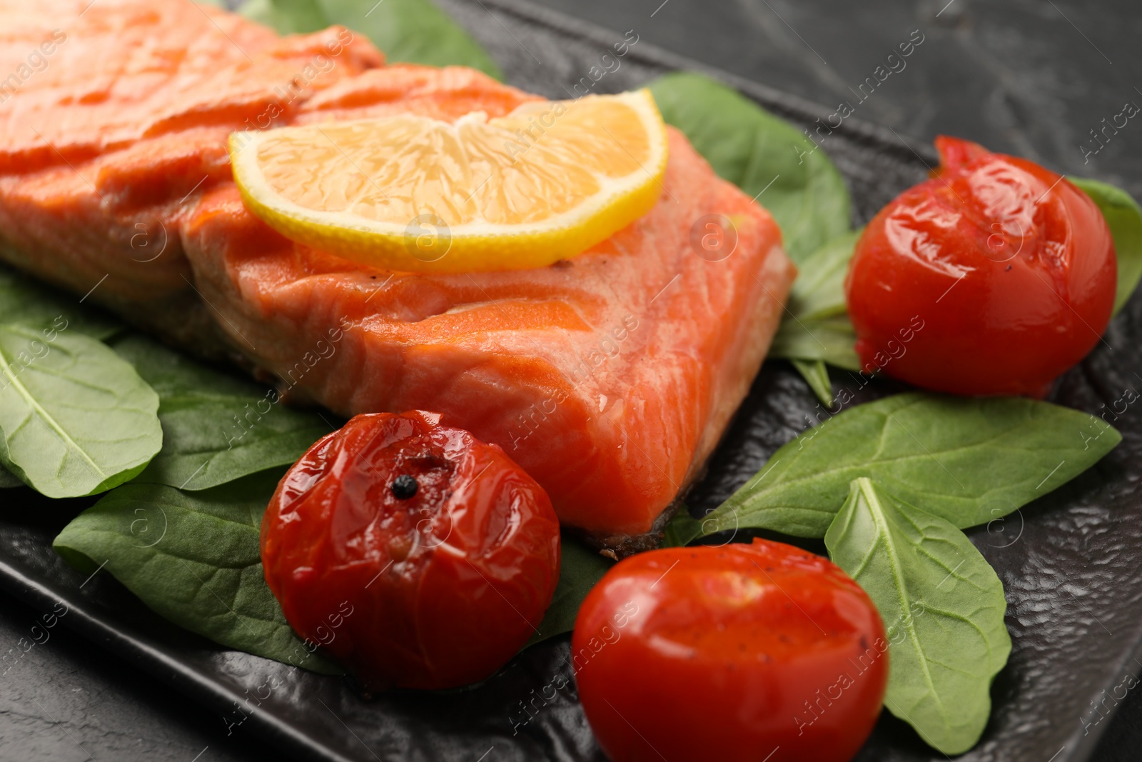 Photo of Tasty grilled salmon with tomatoes, spinach and lemon on table, closeup