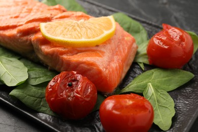 Tasty grilled salmon with tomatoes, spinach and lemon on table, closeup