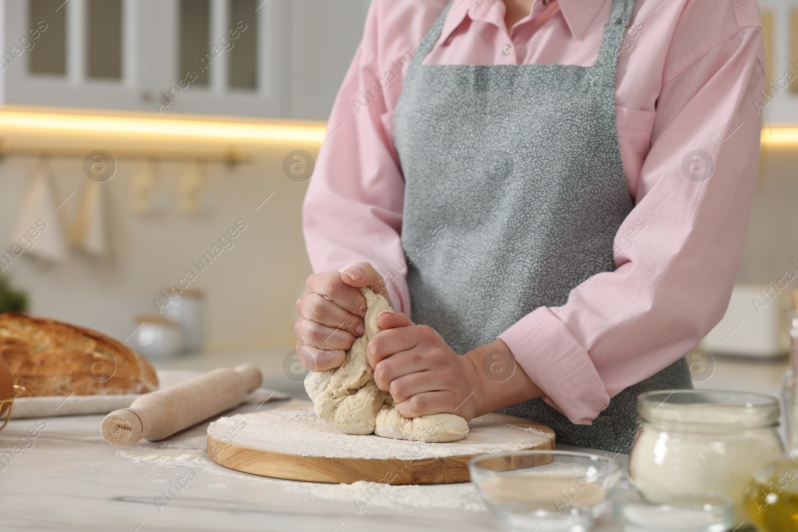 Photo of Making bread. Woman kneading dough at white table in kitchen, closeup