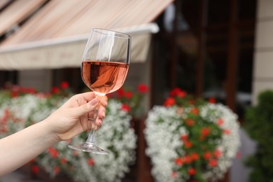 Photo of Woman holding glass of rose wine outdoors, closeup. Space for text