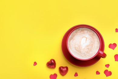 Cup of coffee, chocolate candies and paper hearts on yellow background, flat lay with space for text. Valentine's day breakfast