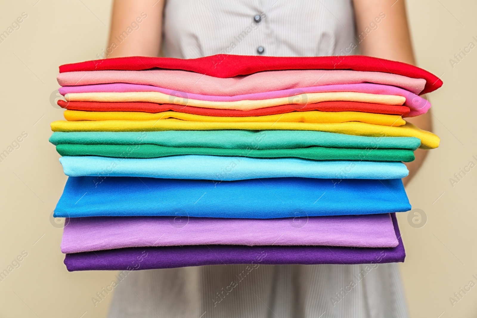 Photo of Woman holding stack of colorful t-shirts on light background