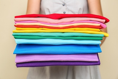 Photo of Woman holding stack of colorful t-shirts on light background