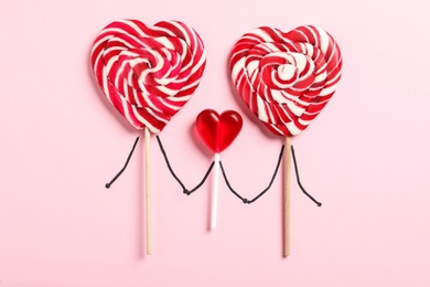 Photo of Flat lay composition with sweet heart shaped lollipops as happy family on pink background