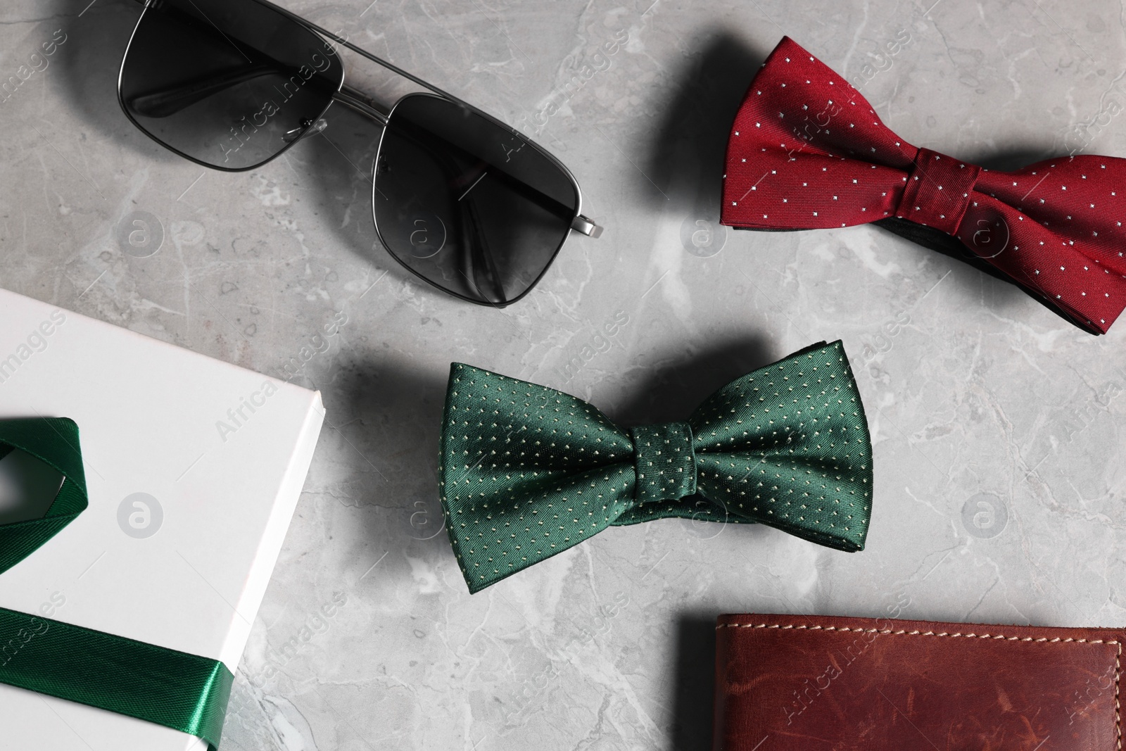 Photo of Stylish color bow ties, box, wallet and sunglasses on gray marble background, flat lay