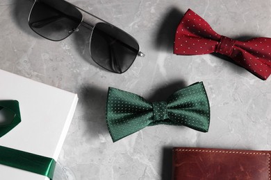 Stylish color bow ties, box, wallet and sunglasses on gray marble background, flat lay