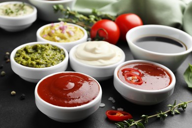 Photo of Different tasty sauces in bowls and ingredients on black table, closeup