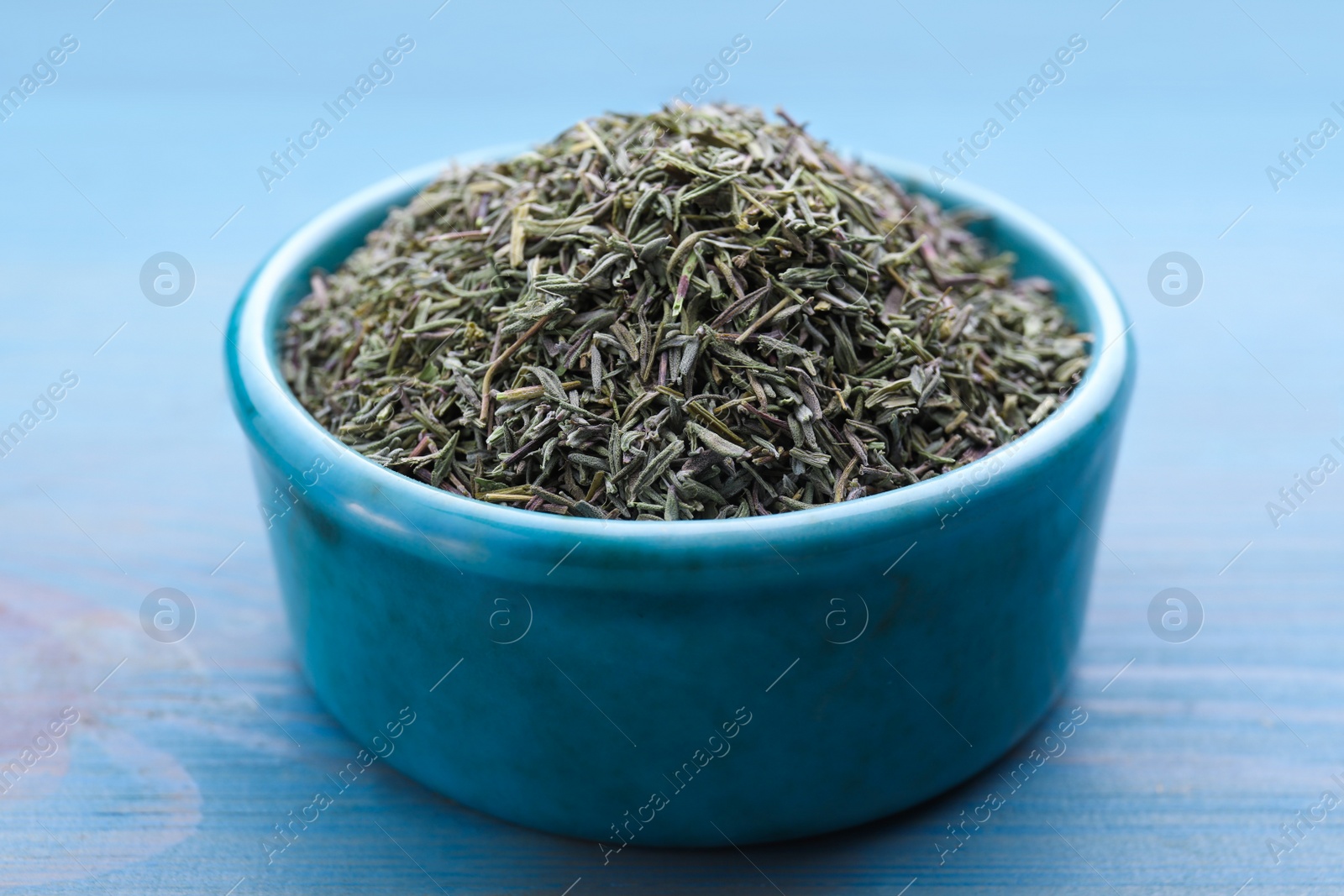 Photo of Ceramic bowl with dried thyme on light blue wooden table, closeup