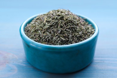 Ceramic bowl with dried thyme on light blue wooden table, closeup