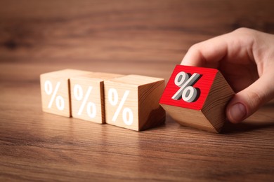 Image of Best mortgage interest rate. Woman putting red cube with percent sign to others on wooden table, closeup