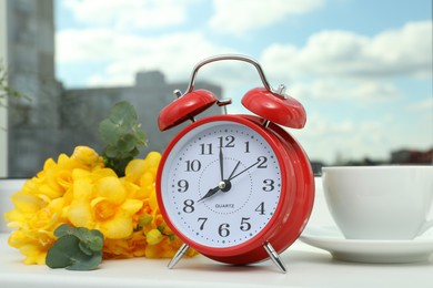 Photo of Alarm clock, beautiful yellow freesias and cup of drink on windowsill. Good morning