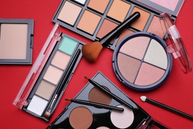 Photo of Colorful contouring palettes with brushes on red background, flat lay. Professional cosmetic product