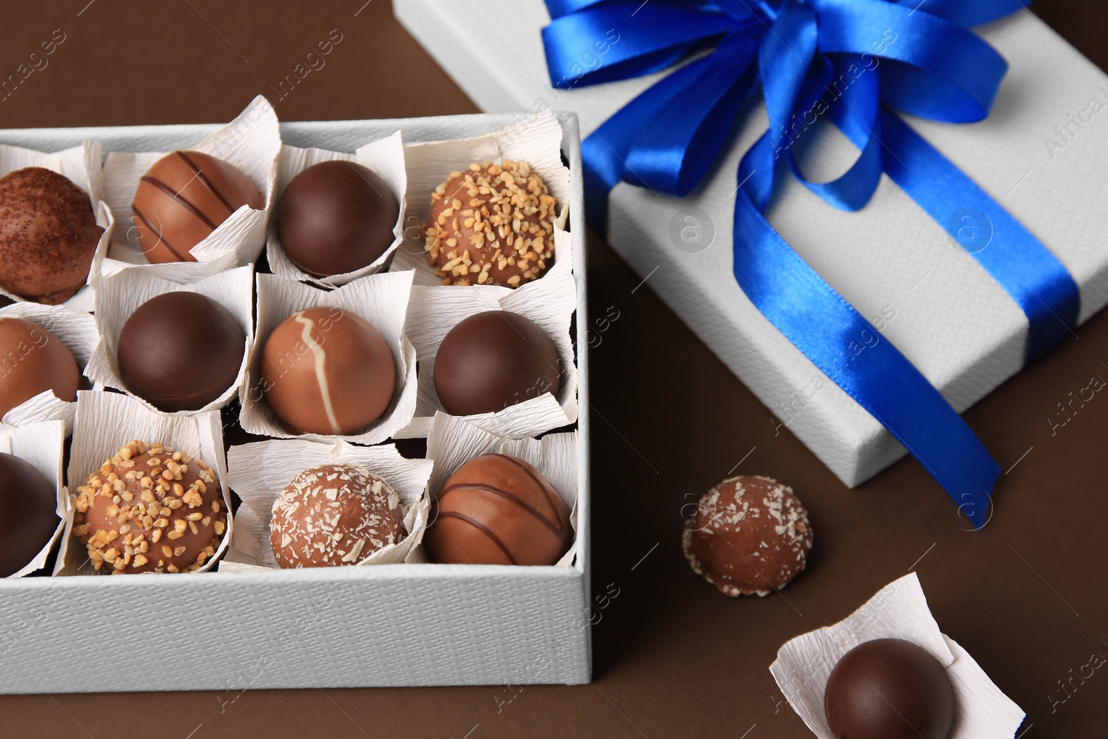 Photo of Box with delicious chocolate candies on brown background, closeup