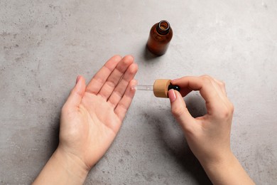 Photo of Woman dripping serum from pipette on her hand at grey table, top view