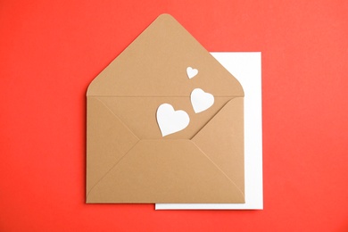 Photo of Envelope with card and paper hearts on red background, top view. Love letter