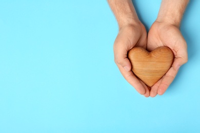 Young man holding wooden heart on light blue background, top view with space for text. Donation concept