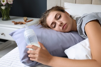 Photo of Exhausted young mother with bottle of milk sleeping in bed at home