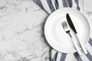 Photo of Empty plate with cutlery and fabric on white marble table, flat lay. Space for text