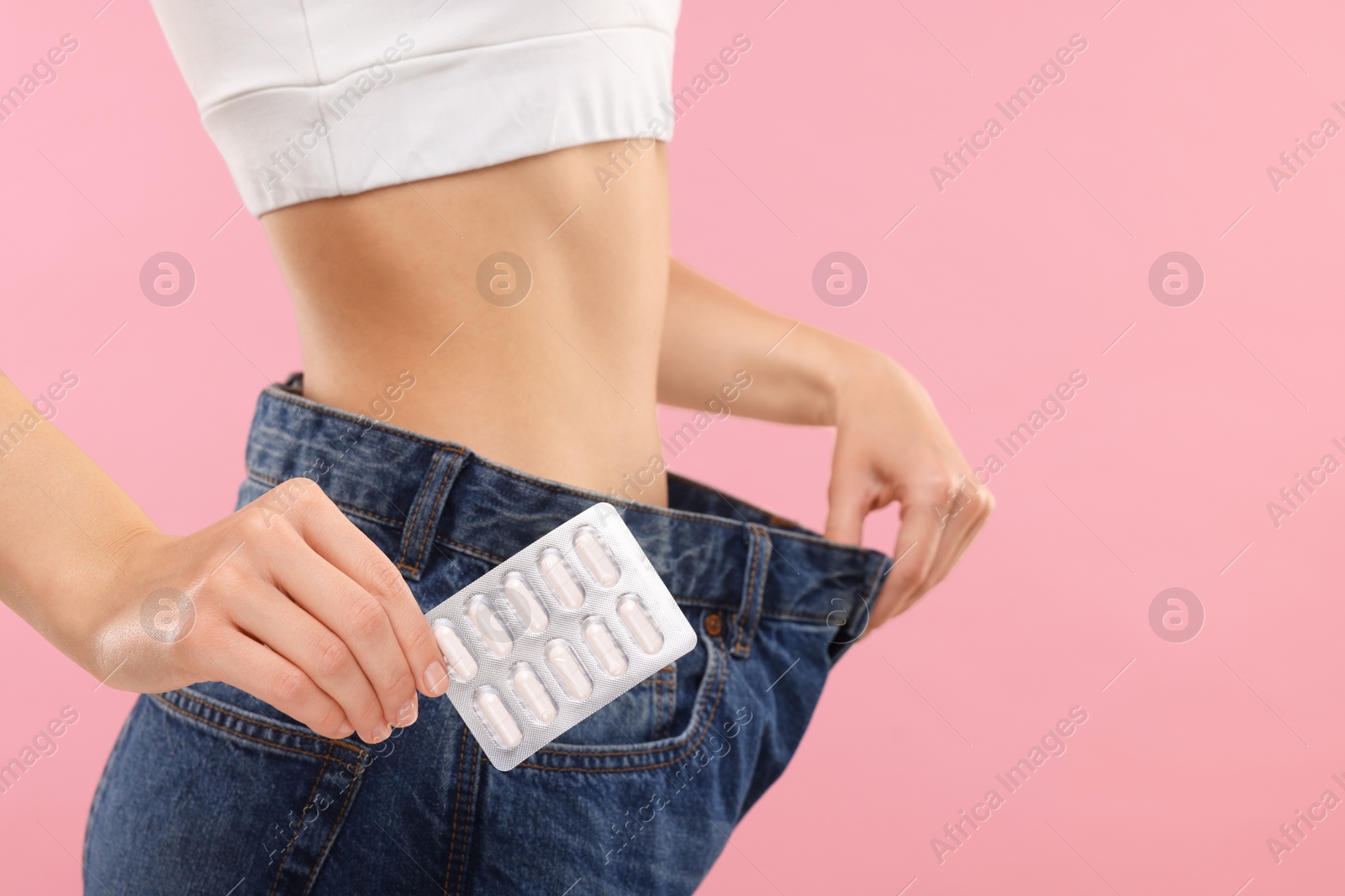 Photo of Slim woman in big jeans with pills on pink background, closeup and space for text. Weight loss