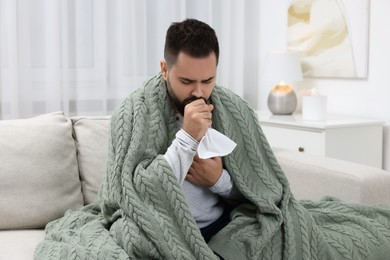 Photo of Sick man with tissue coughing at home