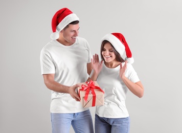 Man presenting Christmas gift to his girlfriend on light background