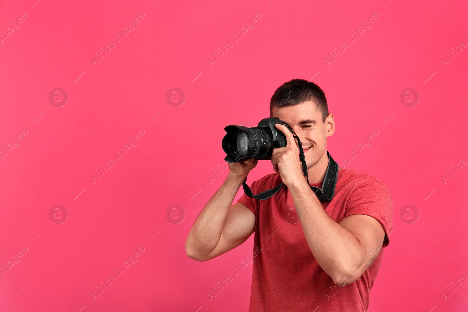 Photo of Young professional photographer taking picture on pink background. Space for text