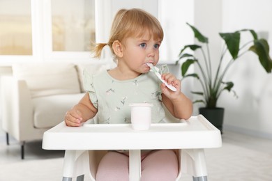 Cute little child eating tasty yogurt with spoon at home