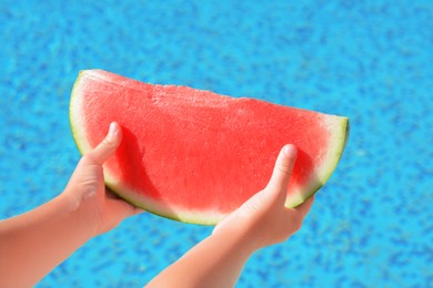 Photo of Child holding fresh juicy watermelon near swimming pool outdoors, closeup