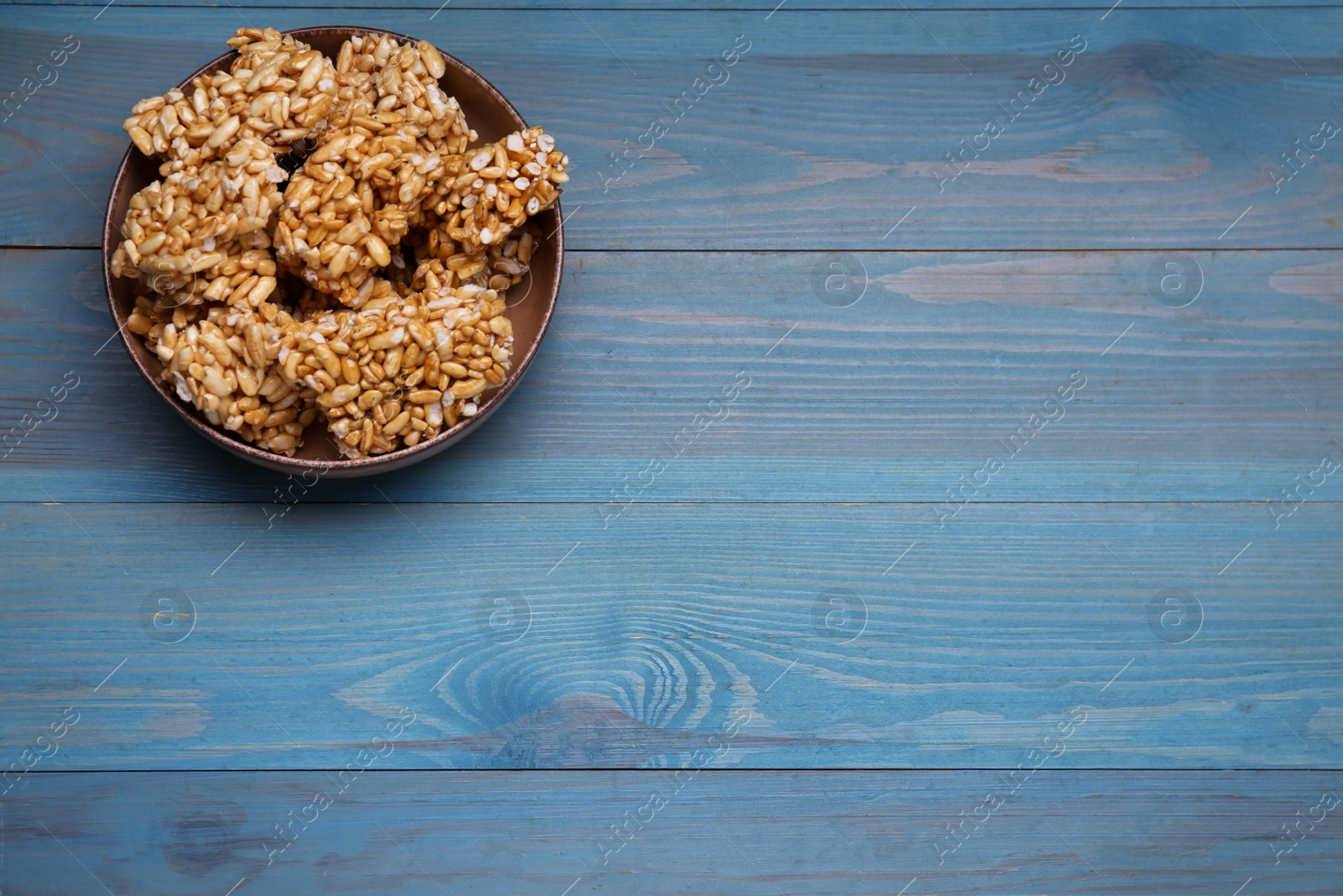 Photo of Bowl of puffed rice bars (kozinaki) on light blue wooden table, above view. Space for text