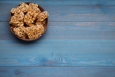 Bowl of puffed rice bars (kozinaki) on light blue wooden table, above view. Space for text