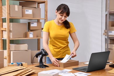 Photo of Parcel packing. Post office worker sticking barcode on box at wooden table indoors