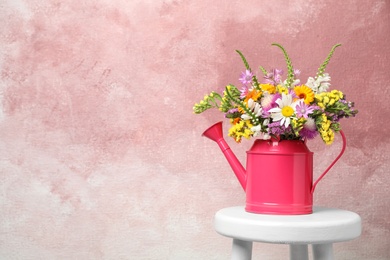 Watering can with beautiful wild flowers on table against color background