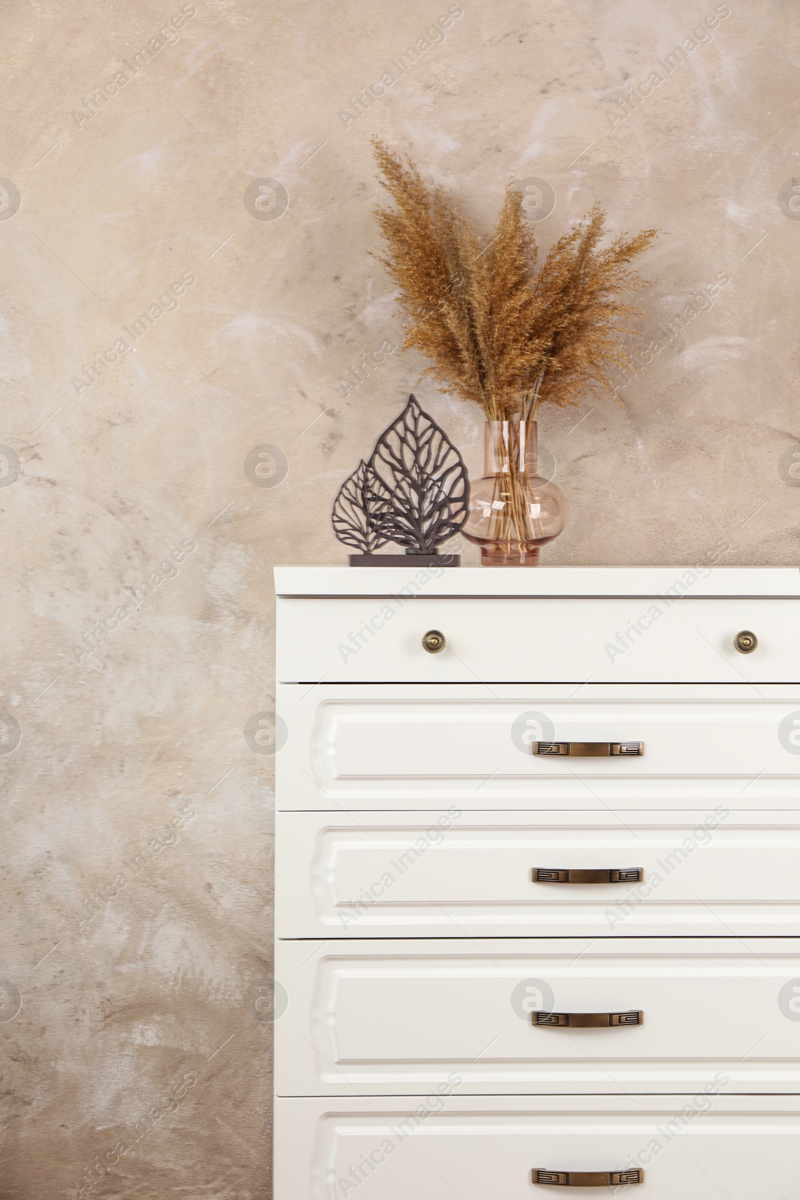 Photo of Modern chest of drawers with decor near beige wall