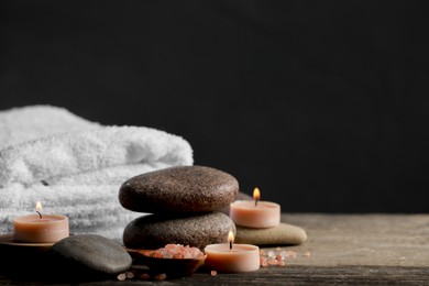 Photo of Beautiful composition with spa stones and burning candles on wooden table against black background. Space for text