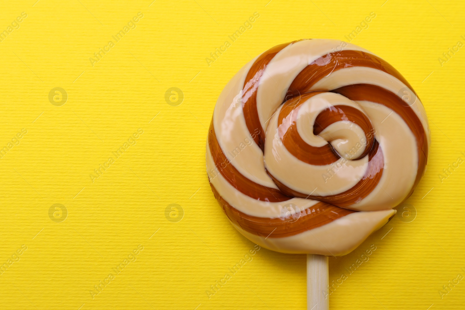 Photo of Delicious lollipop on yellow background, top view. Space for text