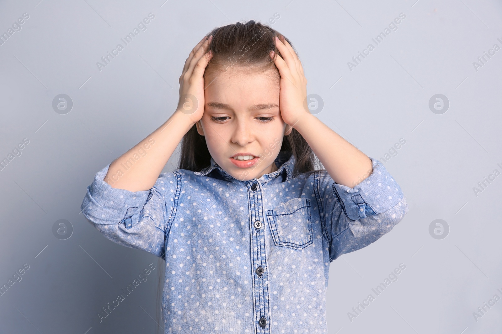 Photo of Little girl suffering from headache on grey background