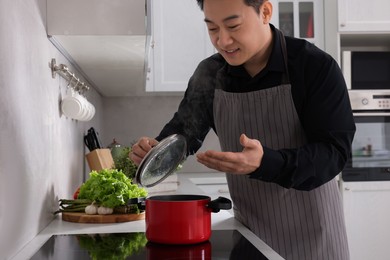 Photo of Man cooking and smelling dish on cooktop in kitchen
