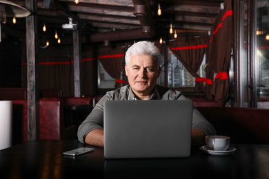 Photo of Senior business owner working with laptop in his restaurant