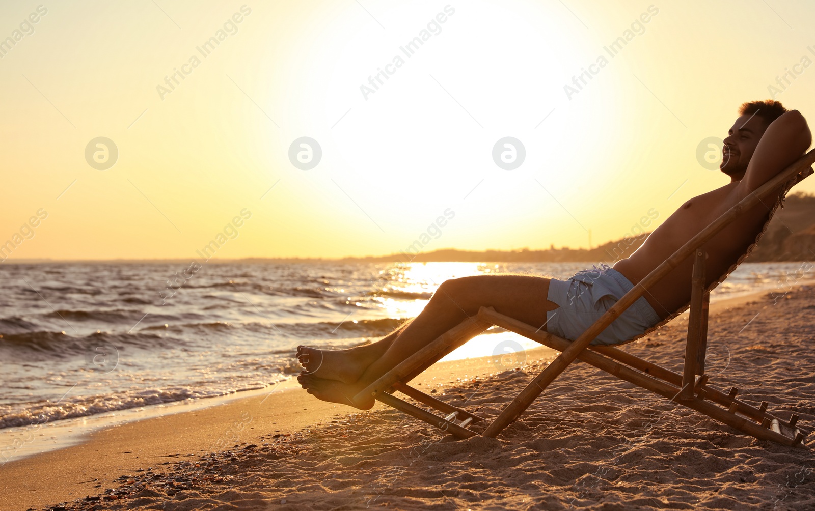 Photo of Young man relaxing in deck chair on beach near sea