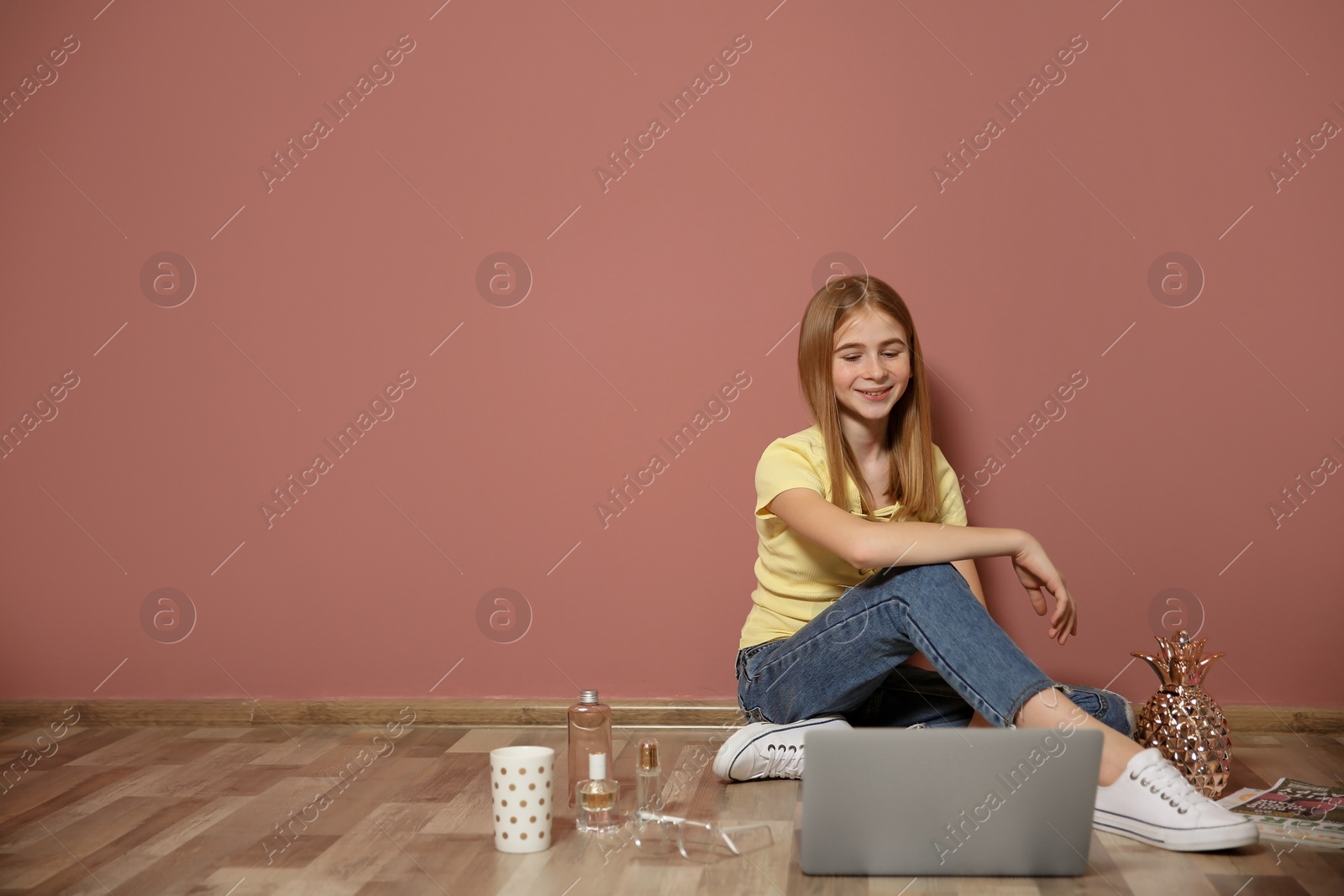 Photo of Cute teenage blogger with laptop sitting on floor against color wall