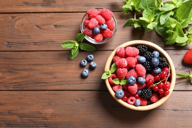 Photo of Bowl with raspberries and different berries on wooden table, top view