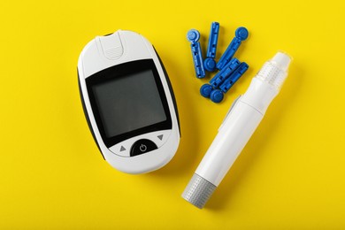 Photo of Digital glucometer, lancets and pen on yellow background, flat lay. Diabetes control