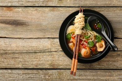 Delicious ramen with chopsticks and spoon in bowl on wooden table, top view with space for text. Noodle soup