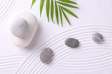 Photo of Zen garden stones and green leaves on white sand with pattern, flat lay